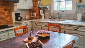 A kitchen with a wooden table, chairs, a coffee maker, a kettle, and a cookbook on the counter.