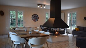 A spacious living room with a large fireplace, a dining area with white chairs, and a sofa.