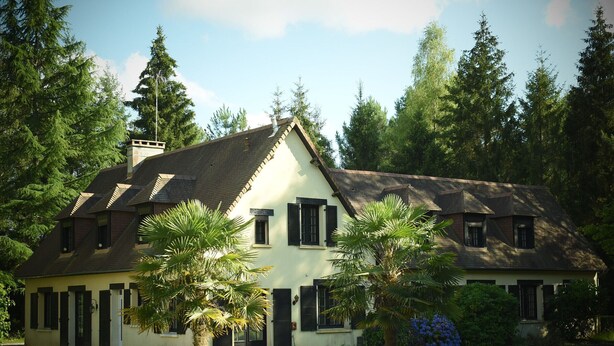 A two-story house with a sloped roof, multiple windows, and a chimney.