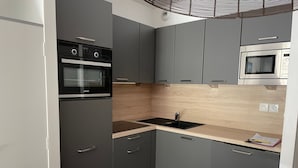 Una cocina compacta con gabinetes grises, un horno negro, un microondas y un lavamanos.