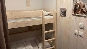 Una cama litera con escalera, un pequeño estante con una imagen de un oso y un interruptor de luz en la pared.