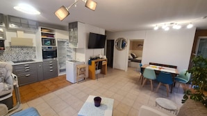 Ett modernt kök med inbyggd ugn, mikrovågsugn och kylskåp. Här finns en matplats med bord och stolar, ett litet skrivbord med en stol och en tv som är monterad på väggen.