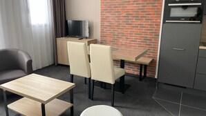 Een moderne hotelkamer met een zithoek, een televisie op een houten kast, een accentmuur van baksteen en een kitchenette.