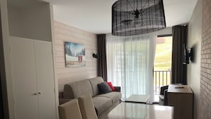 Une chambre d’hôtel moderne, dotée d’un canapé, d’une table à plateau en verre, d’une télévision et offrant une vue sur l’extérieur.