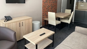 Une chambre moderne dotée d’un bureau en bois, d’un téléviseur fixé au mur, d’un mur décoratif en briques et d’une kitchenette équipée d’un four à micro-ondes.