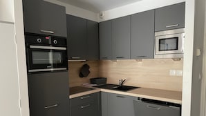 Une cuisine de taille réduite avec des meubles gris, un four noir, un micro-ondes et un évier.
