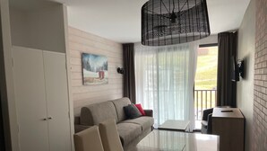A modern hotel room with a sofa, a glass-top table, a TV, and a view of the outdoors. - Studio for 4 in Gourette, southwest balcony, pets allowed (Gourette)