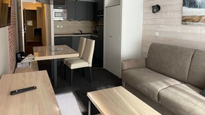 A compact living space with a kitchenette, a sofa, a dining table, and a remote control on the table. - Studio for 4 in Gourette, southwest balcony, pets allowed (Gourette)