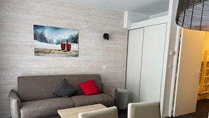 Ett modernt vardagsrum med en grå soffa, ett litet träbord och ett soffbord. På väggen hänger en tavla som föreställer ett snöigt landskap.
