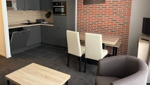 Ett modernt kök med grå skåp, en mikrovågsugn och en ugn. Här finns också en matplats med ett bord och stolar, samt en vägg av tegelsten.