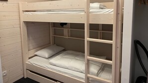 En våningssäng med en stege, vita sängkläder och en väggmonterad lampa.
