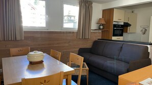 A compact living space with a dining table, chairs, a sofa, and a kitchenette. - Gourette: Duplex Studio 7 pers, Pool & WIFI (Gourette)