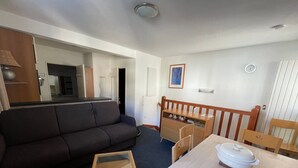 A compact living space with a sofa, a small wooden table, a chair, and a kitchenette area. - Gourette: Duplex Studio 7 pers, Pool & WIFI (Gourette)