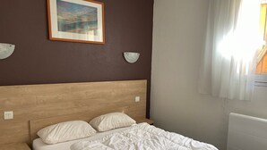 Un lit bien fait, avec une tête de lit en bois, un tableau encadré au mur et une table de chevet avec une lampe.