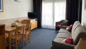 Une chambre d’hôtel de taille modeste, comprenant une table à manger, des chaises, un canapé, un téléviseur et une grande fenêtre avec des rideaux.
