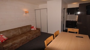 A compact living space with a brown sofa, a small dining table, and a kitchen area. - Comfort studio 6 ppl, terrace, pets allowed, sheets included (Gourette)
