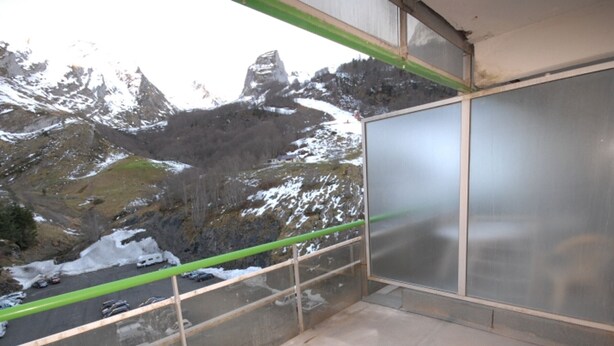 A balcony with a view of snow-covered mountains and a road with vehicles. - Comfort studio 6 ppl, terrace, pets allowed, sheets included (Gourette)