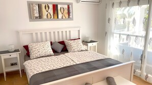 Ein Schlafzimmer mit Bett, Nachttischen, Fenster mit Blick und einer Wand-Klimaanlage.