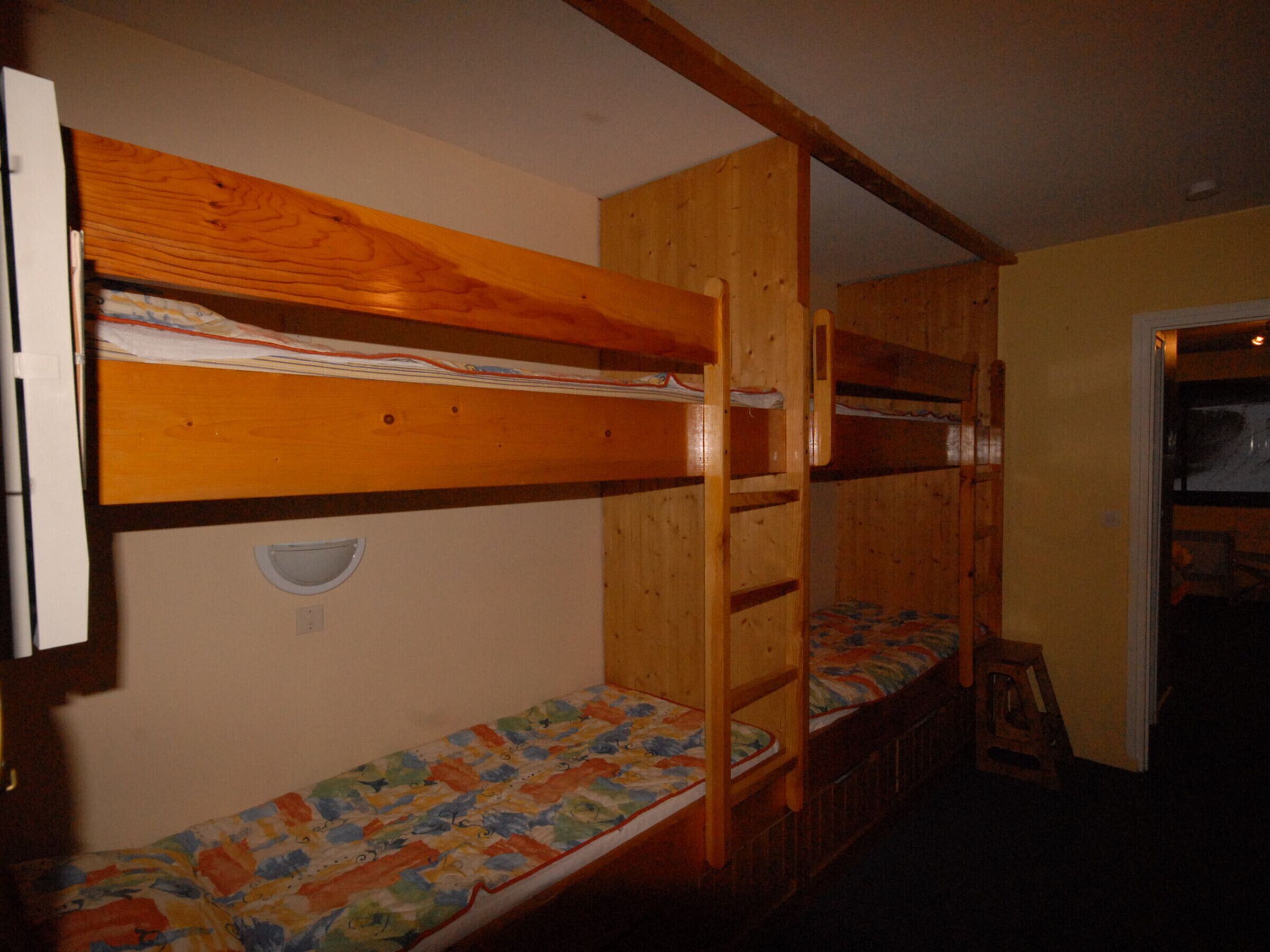 Dormitori amb lliteres, parets de fusta i una porta que dona a una altra habitació.