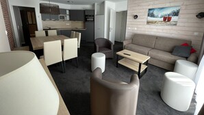 Quarto de hotel moderno com área de jantar, sofá, mesa de centro e cozinha ao fundo.