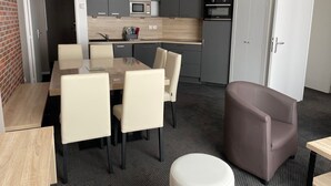 Uma cozinha moderna com armários cinzas, um micro-ondas e um forno. Há uma mesa de jantar com cadeiras e uma pequena mesa redonda com uma cadeira.