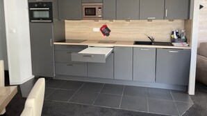 Een kleine keuken met grijze kastjes, een magnetron en een ingebouwde oven.