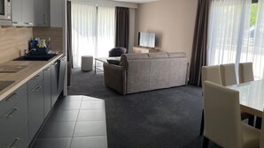 Een moderne hotelkamer met een kitchenette, een bank, een televisie en een eethoek.