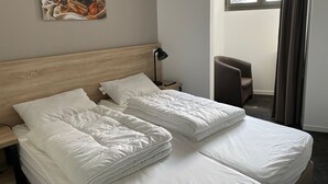 Een hotelkamer met twee bedden, een houten hoofdeinde, een nachtkastje met een lamp, een stoel en een schilderij aan de muur.