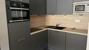 Een moderne keuken met donkere kastjes, een zwarte oven, een magnetron, een spoelbak en een houten achterwand.