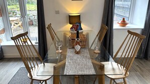 A dining area with a glass table, wooden chairs, a lamp, and a view of the outdoors. - Excellent 2 bed cottage in the stunning Scottish Highlands near Portmahomack (Tain)