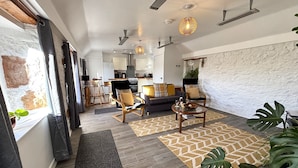 A modern living room with a sofa, coffee table, and chairs. There is a kitchen in the background with cabinets and appliances. - Excellent 2 bed cottage in the stunning Scottish Highlands near Portmahomack (Tain)