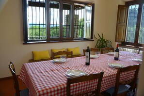 Un comedor con mantel a cuadros, sillas de madera, cojines amarillos y vistas a través de las ventanas.