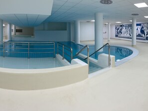 Ein Hallenbad mit blau-weißer Farbgebung, umgeben von weißen Wänden und Säulen, mit Wandgemälden an der Wand.