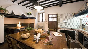 A cozy kitchen with a wooden table set for a meal, a fireplace, and a patterned backsplash. - Villa Storica Volterra (Volterra)