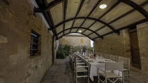 A long table set for dining in a stone-walled building with a vaulted ceiling and a view of a distant building. - Villa Storica Volterra (Volterra)