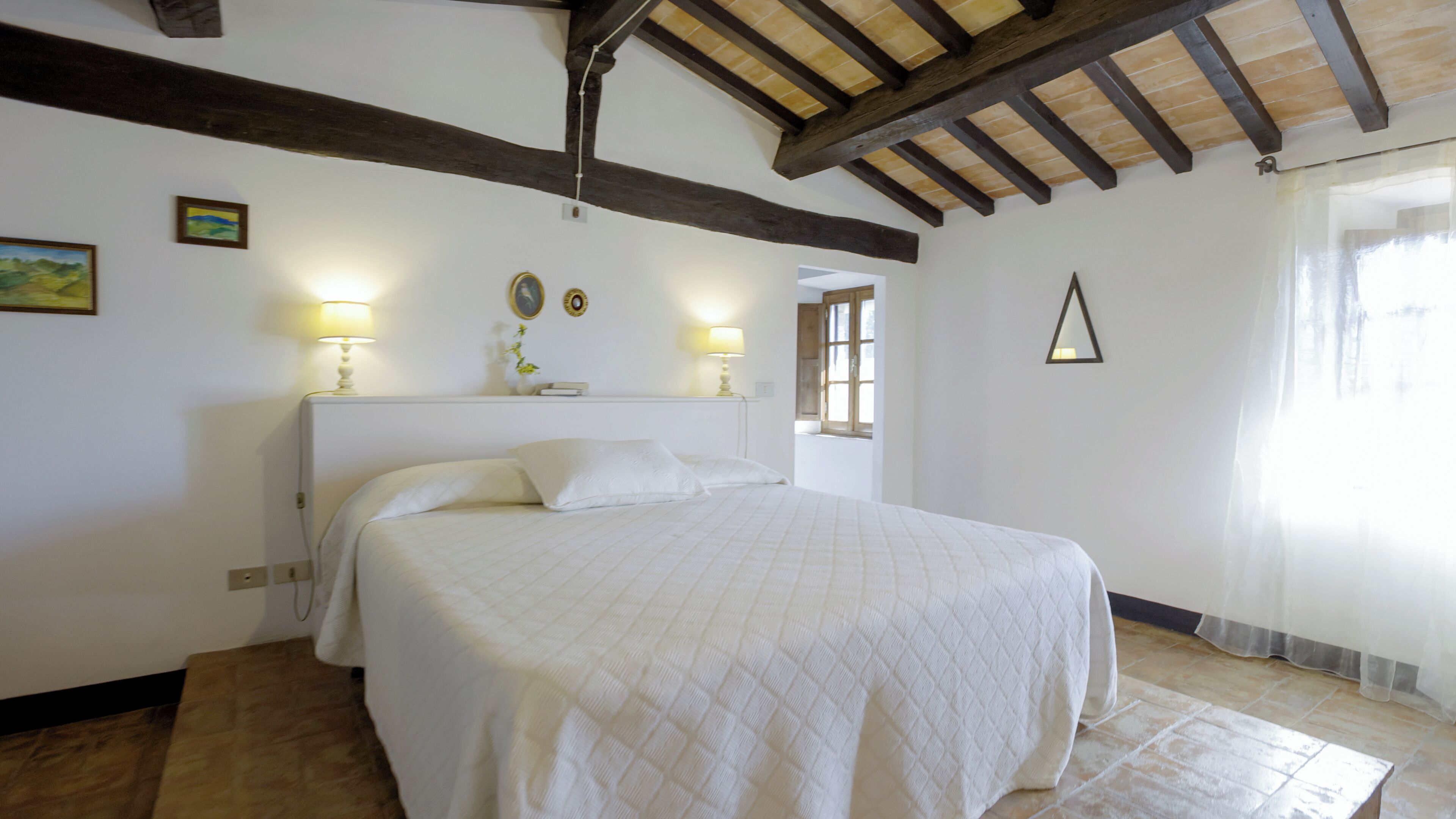 Una camera da letto con un letto grande, travi in legno al soffitto e due lampade ai comodini.