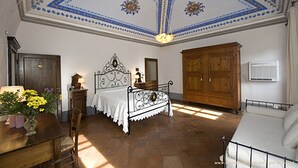 A bedroom with a bed, wooden wardrobe, and a ceiling with blue and white patterns. - Villa Storica Volterra (Volterra)
