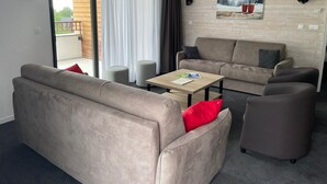 En moderne stue med sofa, lænestole, sofabord og et billede på væggen.