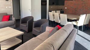 Et moderne opholdsområde med sofa, stole, et spisebord og et køkken i baggrunden.