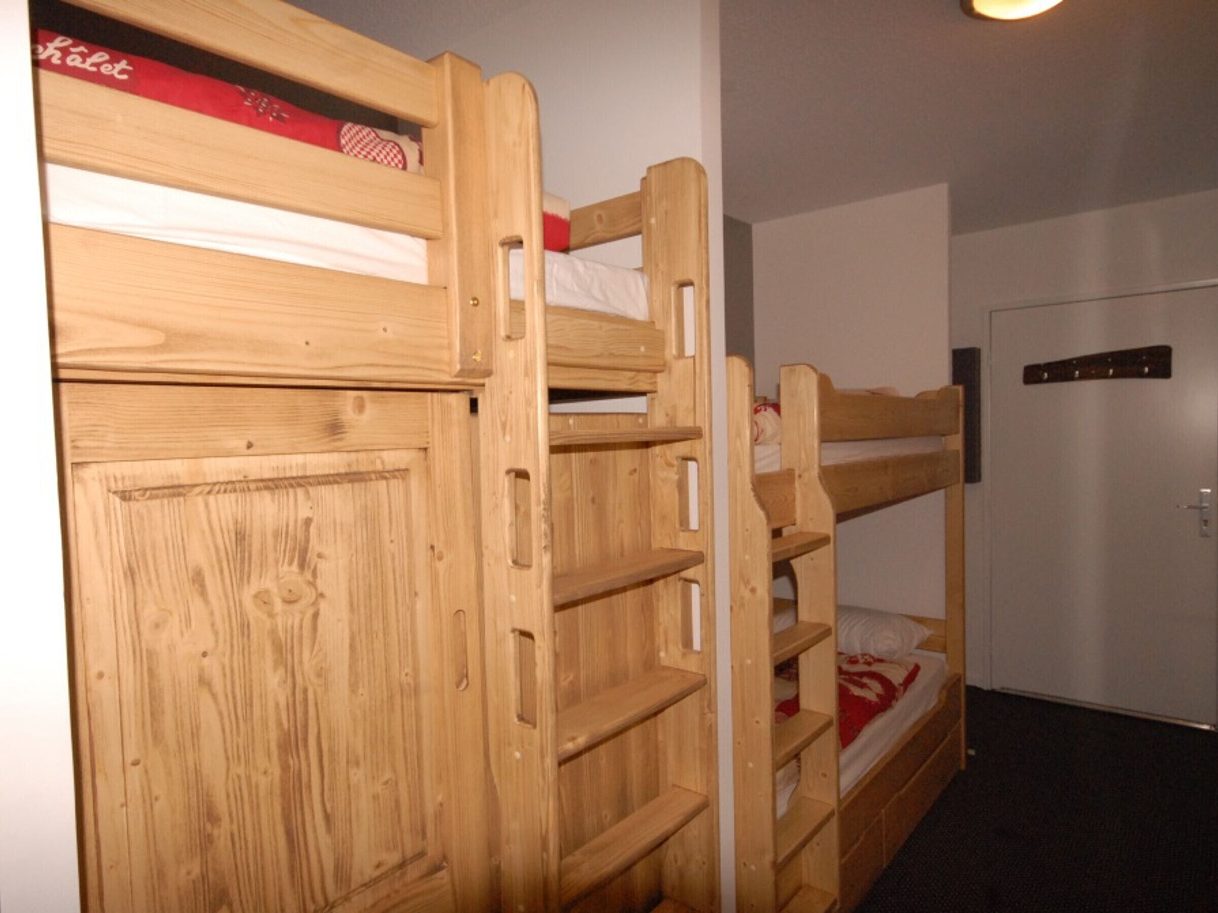 Un lit superposé avec une tête de lit en bois et une porte, un mur blanc et une porte dotée d’une poignée.