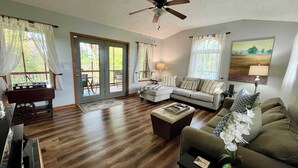 A spacious living room with a wooden floor, a sofa, a coffee table, and a ceiling fan. - Sunfish Cove – Pet-Friendly Lakeside Retreat (Scottsville)
