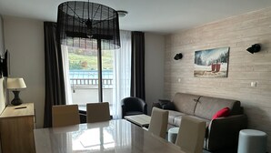 Une chambre d’hôtel moderne équipée d’une table à manger, de chaises, d’un canapé, d’une lampe, d’un tableau et offrant une vue sur l’extérieur.