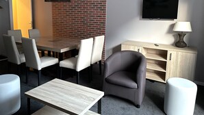 Une chambre d’hôtel moderne avec un mur d’accent en briques, un téléviseur à écran plat, un meuble en bois et un coin repas avec une table et des chaises.