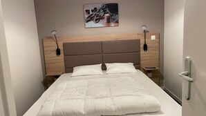 Un lit bien fait, avec une tête de lit, une table de chevet avec une lampe et un tableau accroché au mur.