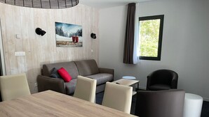 A modern hotel room with a wooden wall, a sofa with red cushions, a dining table, and a window with curtains. - Gourette: 3-room Apt, 8 pers, pool (Gourette)