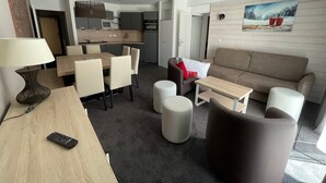 Ein modernes Wohnzimmer mit einer Couch, einem Esstisch mit Stühlen, einer Küchenzeile inklusive Mikrowelle und einem Bild an der Wand.