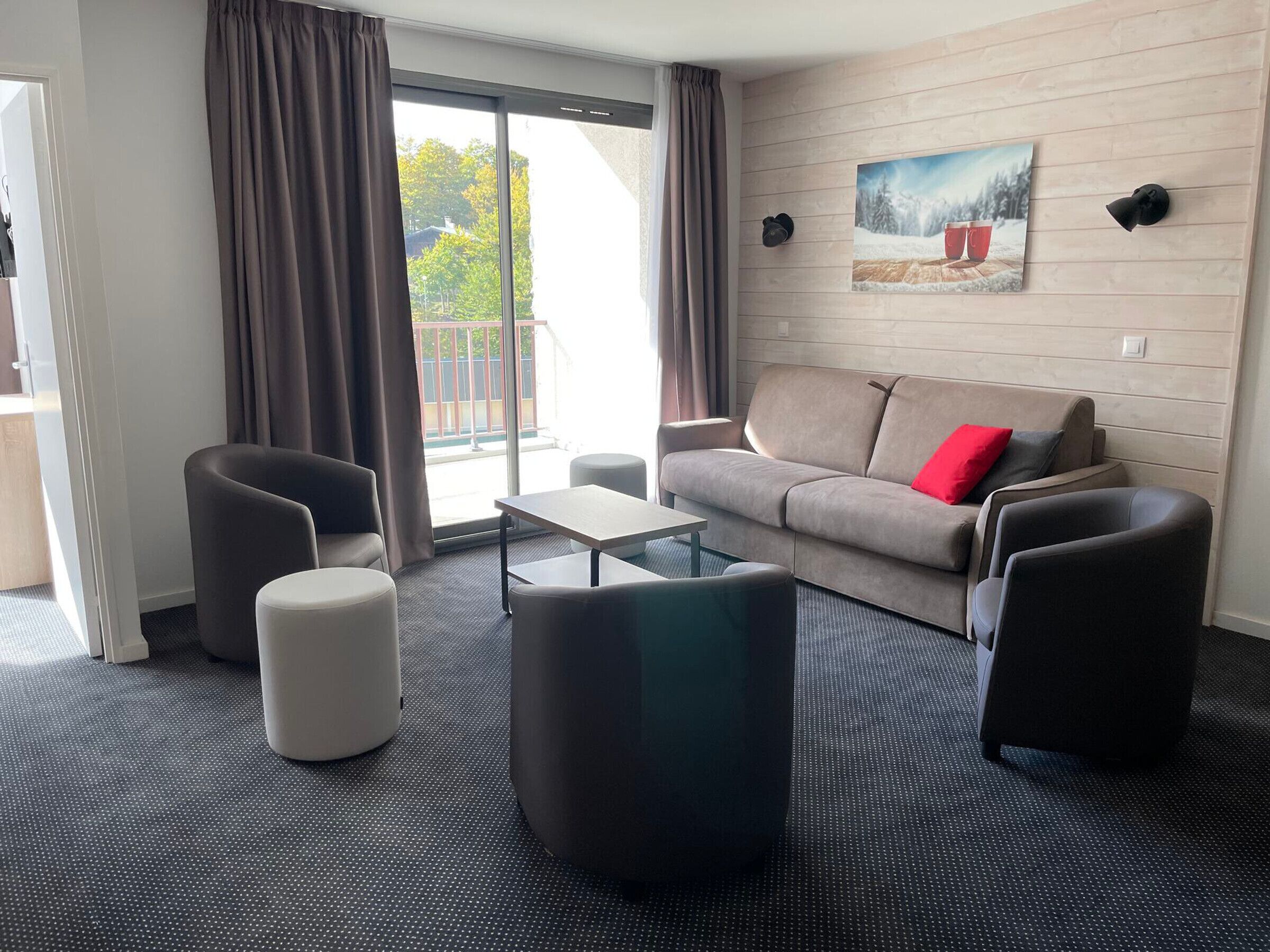 Ein modernes Wohnzimmer mit einer Couch, zwei Sesseln, einem Couchtisch und einem großen Fenster mit Vorhängen.