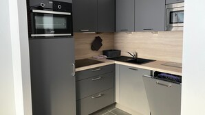 A compact kitchen with grey cabinets, a black oven, a sink, and a dishwasher. - Gourette: Apartment for 8, 56m², Pets Allowed (Gourette)