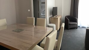 A hotel room with a wooden dining table, four chairs, a television on a wooden cabinet, a grey armchair, and a large window with curtains. - Gourette: Apartment for 8, 56m², Pets Allowed (Gourette)