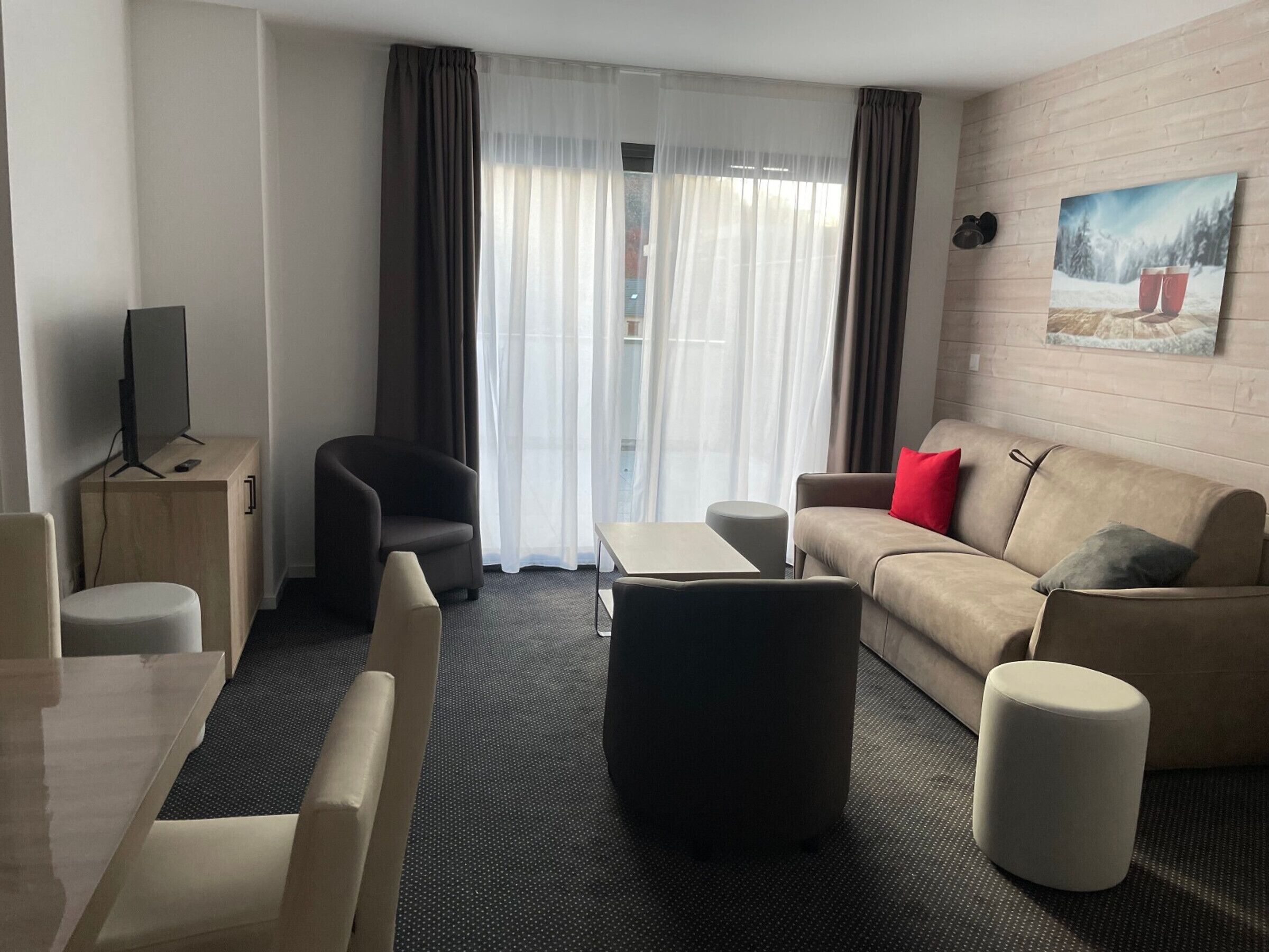A modern living room with a sofa, armchair, ottoman, and a flat-screen TV on a wooden cabinet.